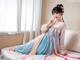 A woman in a blue and pink dress sitting on a bed.